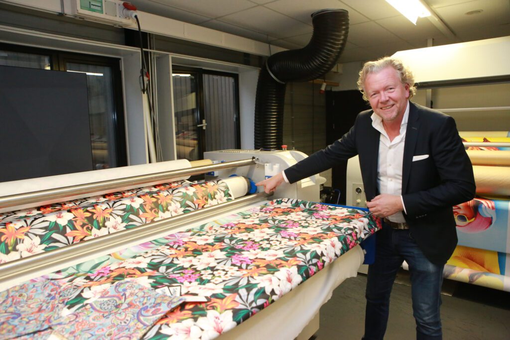 Jorg Schuurman van Klieverik wijst naar de extra rol die ervoor zorgt dat het transferpapier al voor de trommel op het textiel wordt gedrukt.